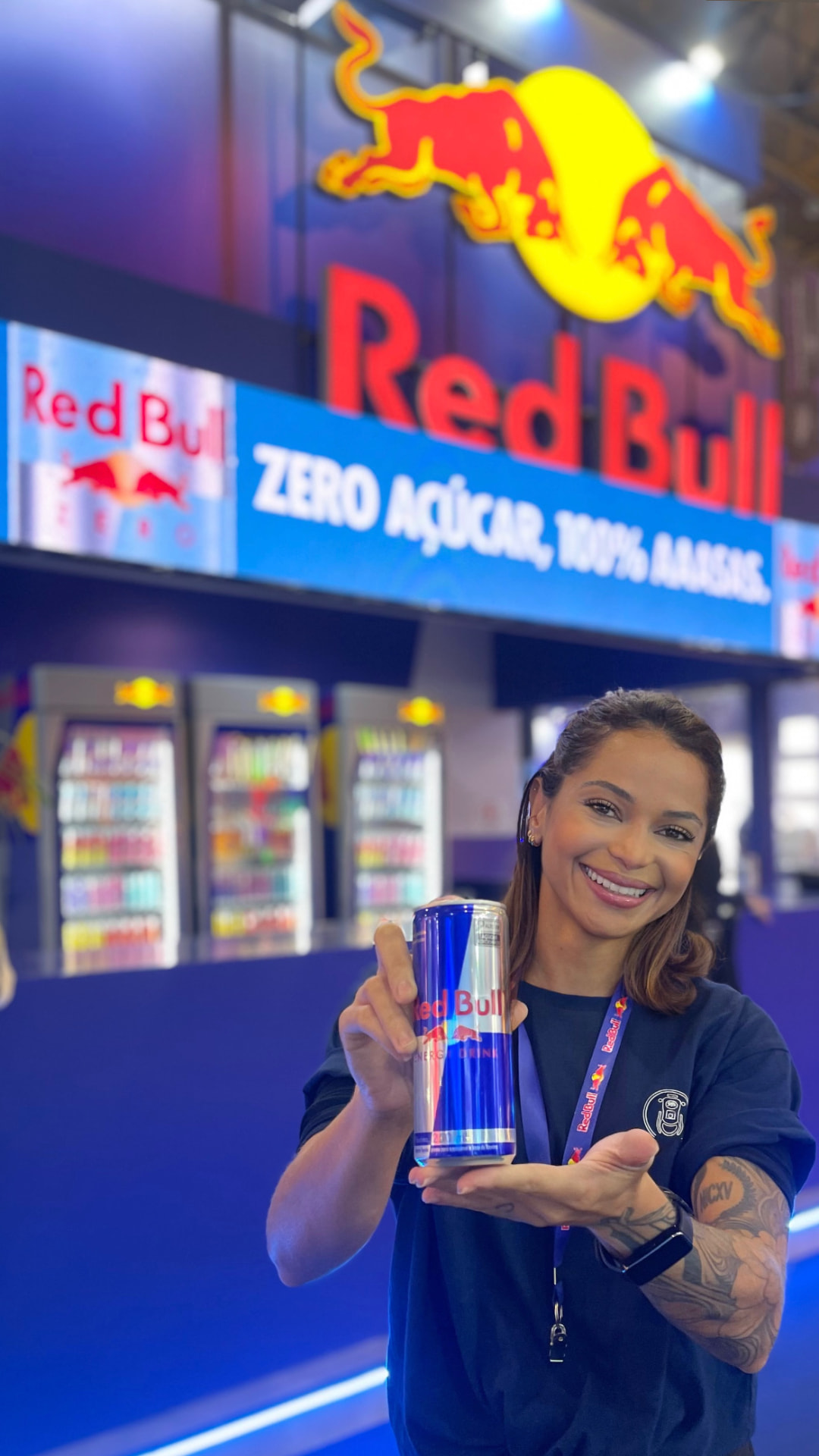 Bárbara Macedo apresentando uma lata Red Bull diante do estande da marca